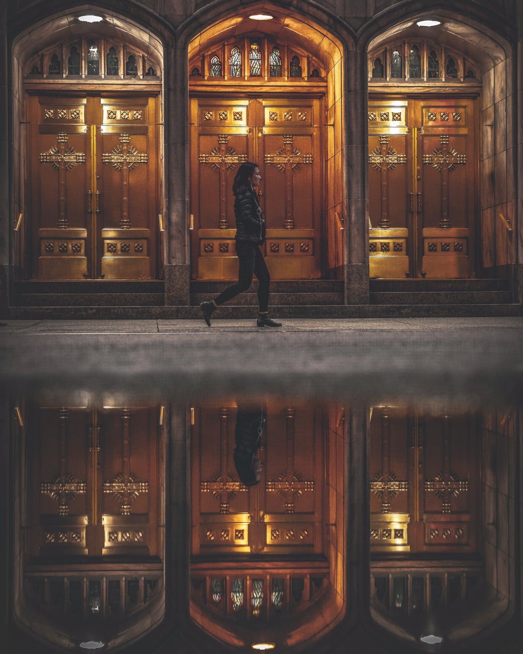 woman walking near closed doors of building near water with self reflection